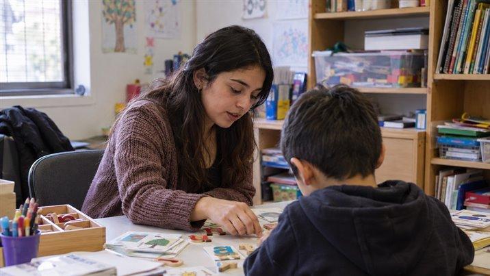 Una educadora ayuda a un niño a ordenar letras de madera y tarjetas sobre una mesa