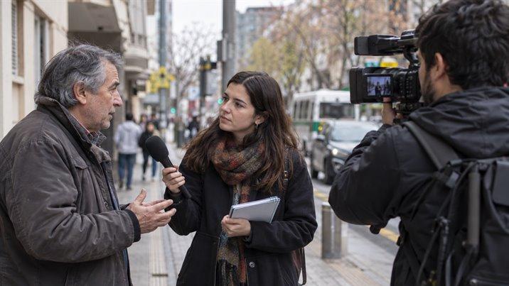 Una periodista entrevista en la calle a un vecino mayor, con un micrófono y una libreta