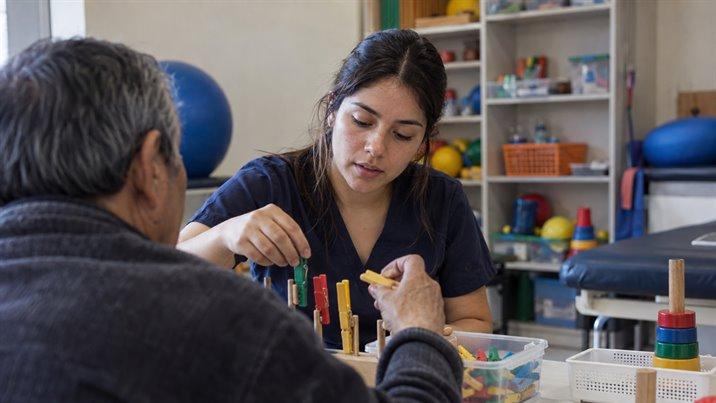 Una terapeuta ocupacional ayuda a un hombre mayor a practicar el agarre con piezas de colores