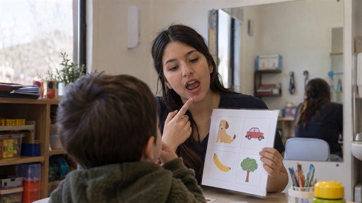 Una fonoaudióloga le muestra una lámina con dibujos a un niño sentado frente a ella