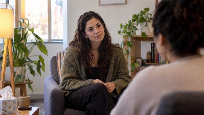 Una psicóloga sentada en un sillón escucha con atención a una persona que está de espaldas